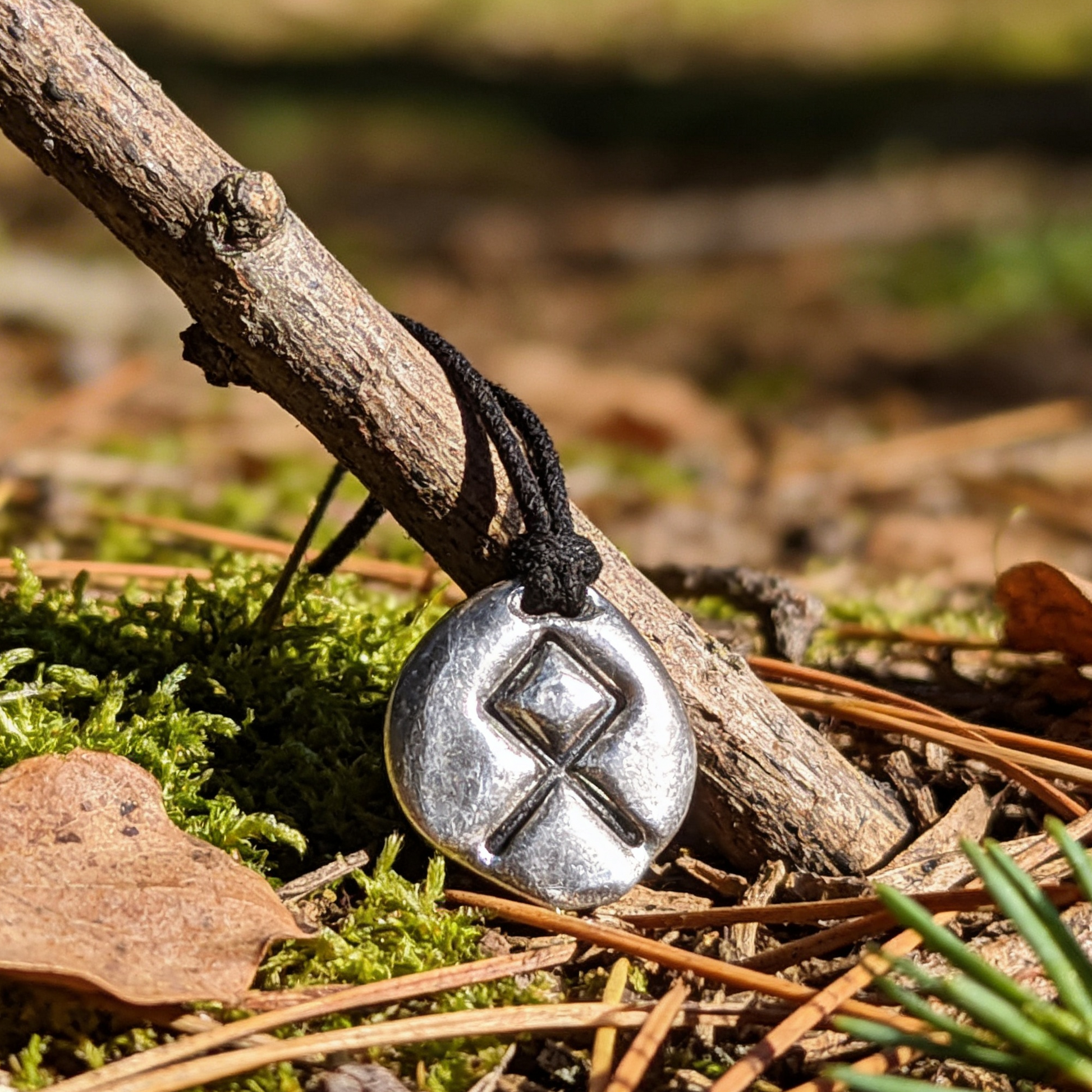 Metal pendant with a runic symbol on a branch in a forest setting